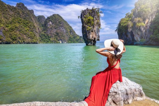A tourist woman in a red dress looks at the famous spot James Bond island, Thailand